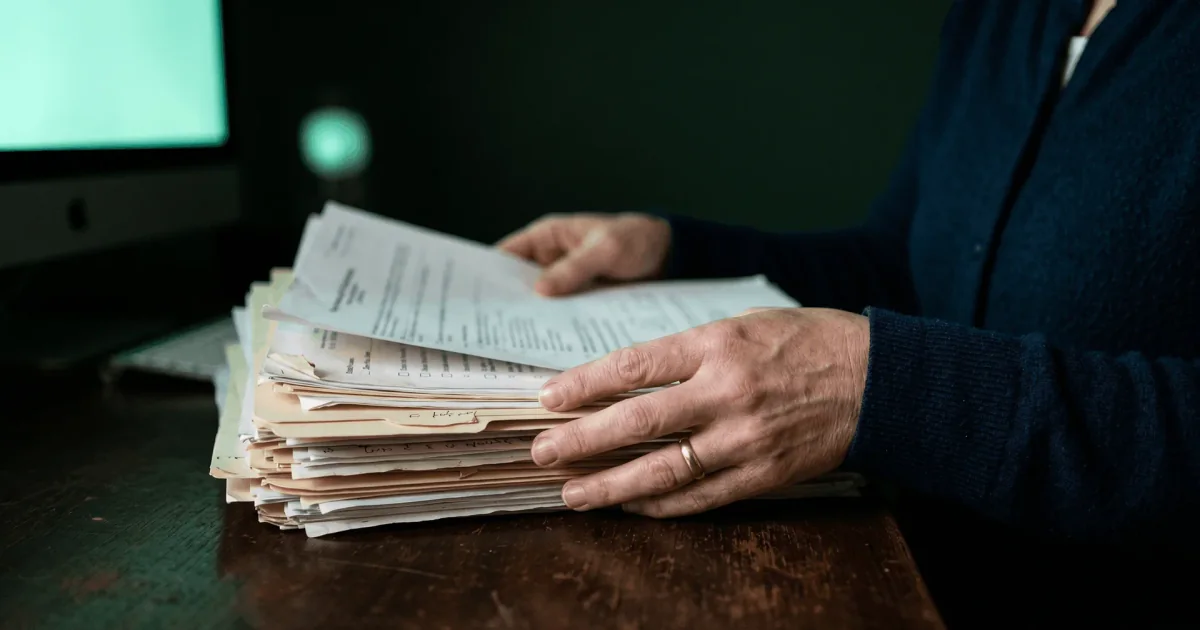 Prior Authorization Automation for FQHCs Coordinator sorting a stack of prior authorization paperwork at a desk