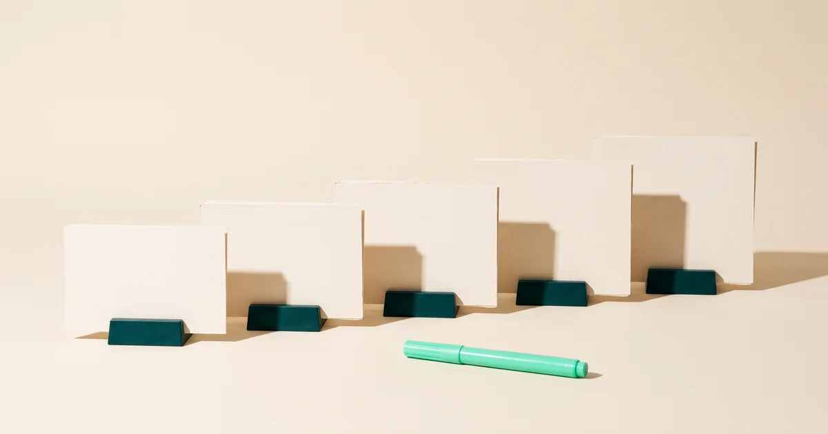 Five blank cards in ascending sizes standing in dark green holders on a cream surface beside a mint marker