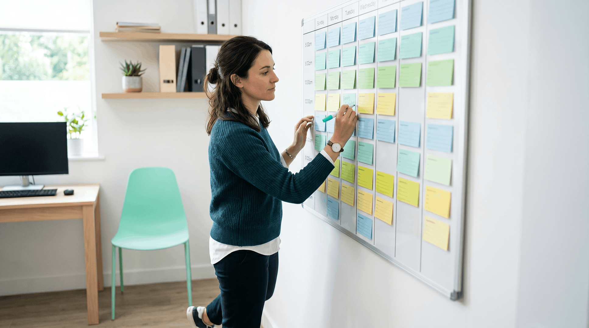 Practice leader in a teal sweater annotating color-coded sticky notes on a large whiteboard schedule — the manual care-gap tracking work that automation replaces, with each note representing an open patient outreach task