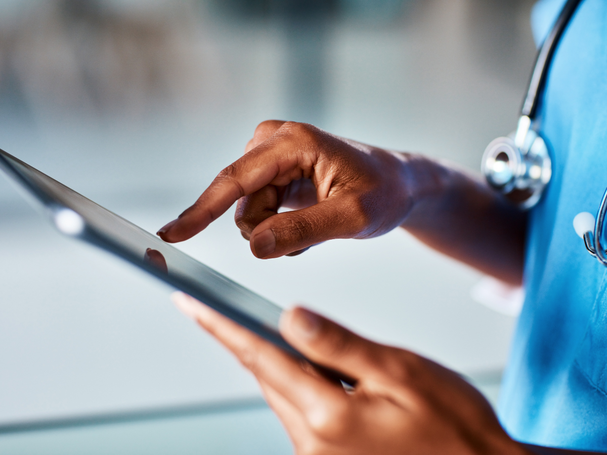 A healthcare worker wearing a stethoscope uses an electronic tablet.